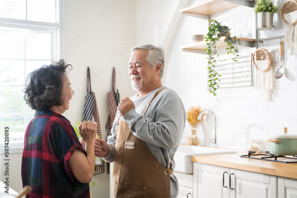 一对亚洲成熟的老年夫妇在家里的厨房里跳舞，面带微笑。