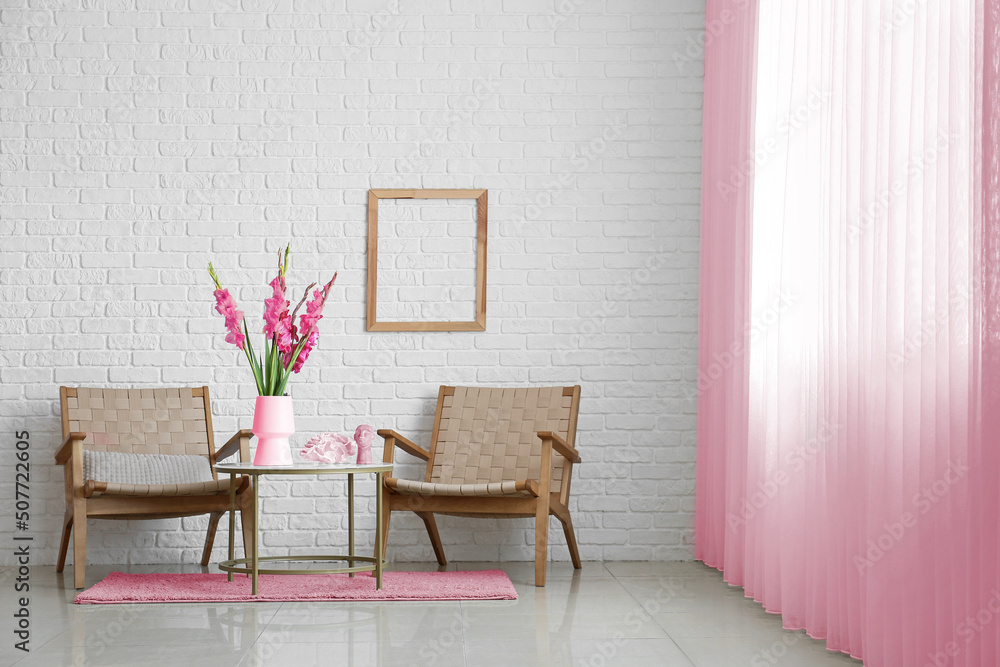 Comfortable armchairs, table and vase with beautiful gladiolus flowers in light room near window