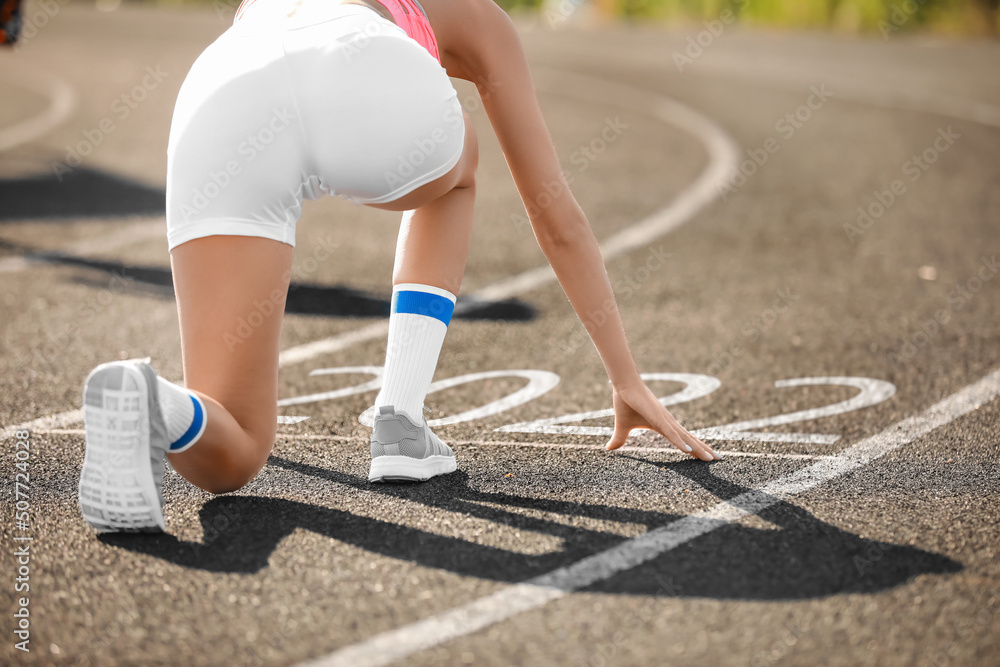 在体育场的跑道上，一名运动型年轻女子以接近2022年的姿势蜷缩着起跑