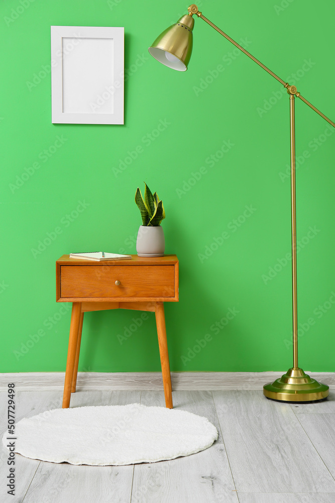 靠近绿色墙壁的带室内植物和标准灯的木桌
