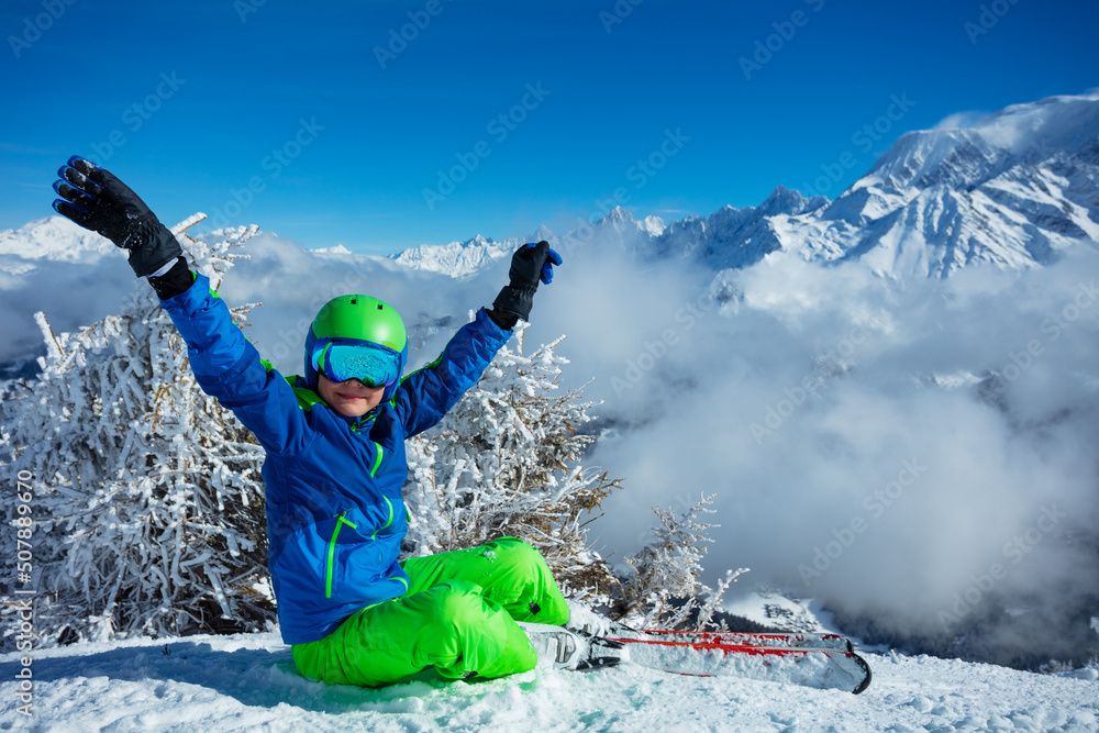 滑雪男孩坐在云端的山顶举起双手