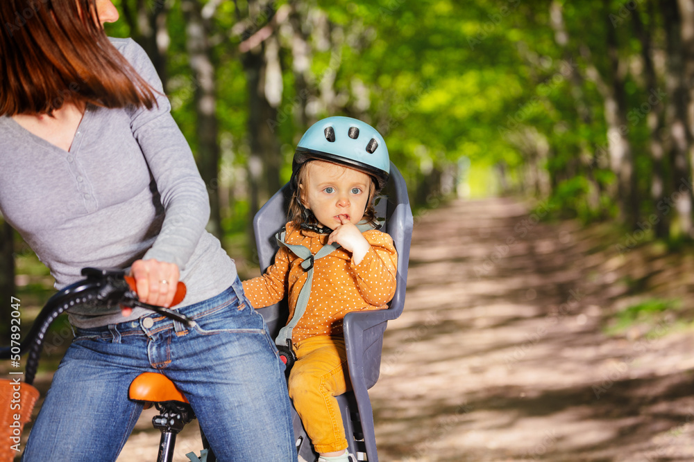 女孩坐在自行车座位上和妈妈在公园里骑行