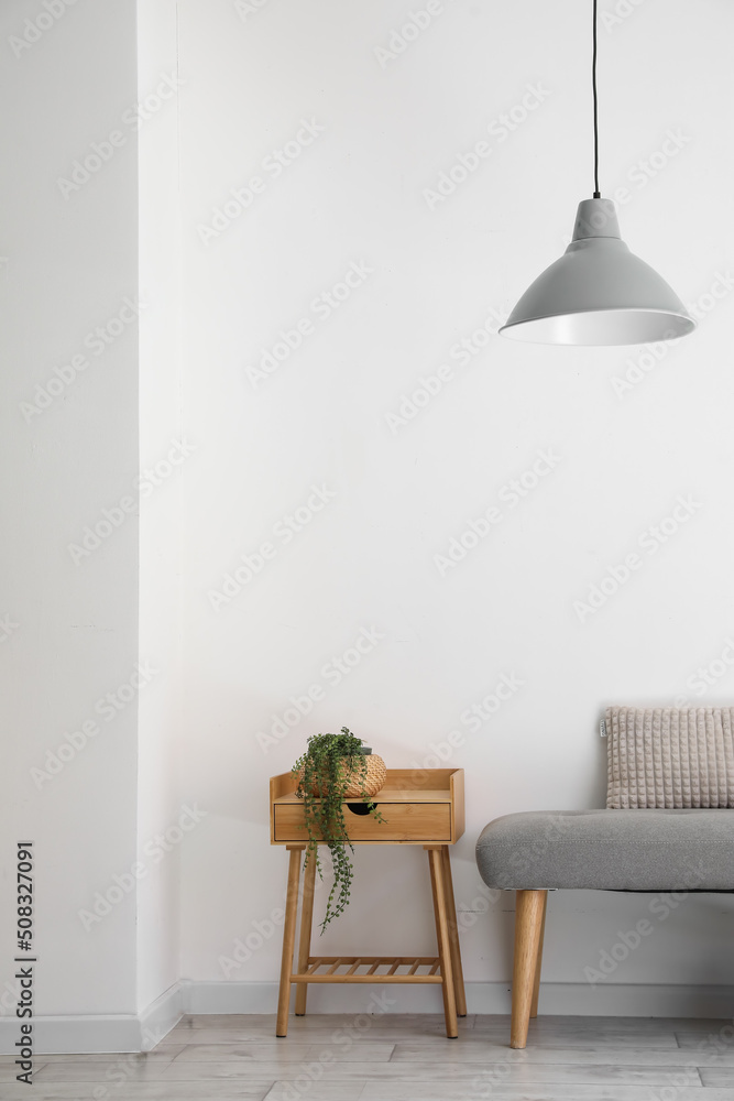 靠近浅色墙壁的带室内植物的软长凳和桌子