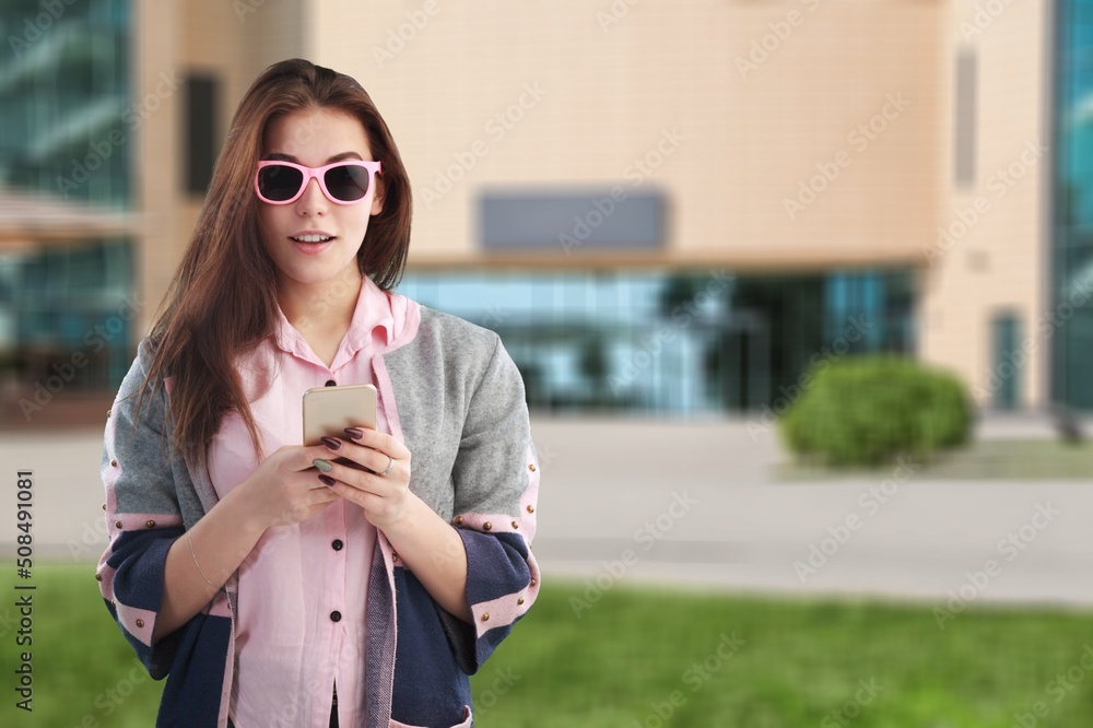 快乐的学生女孩站在户外大学大楼上用手机
