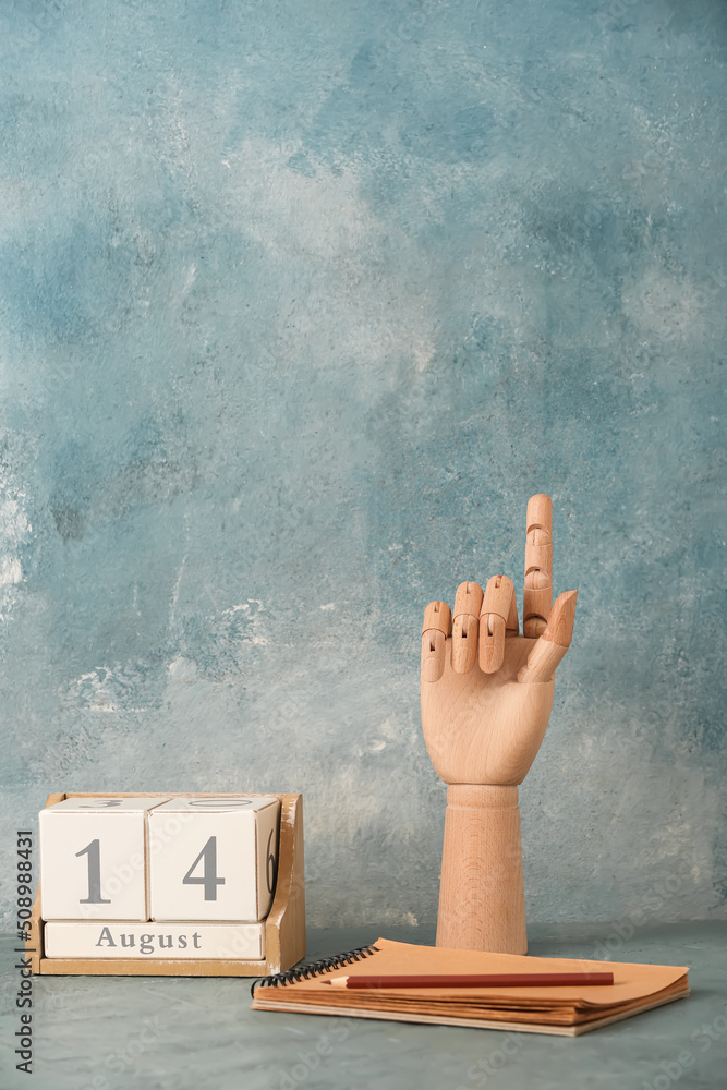 Wooden hand with pencil, notebook and cube calendar on blue background