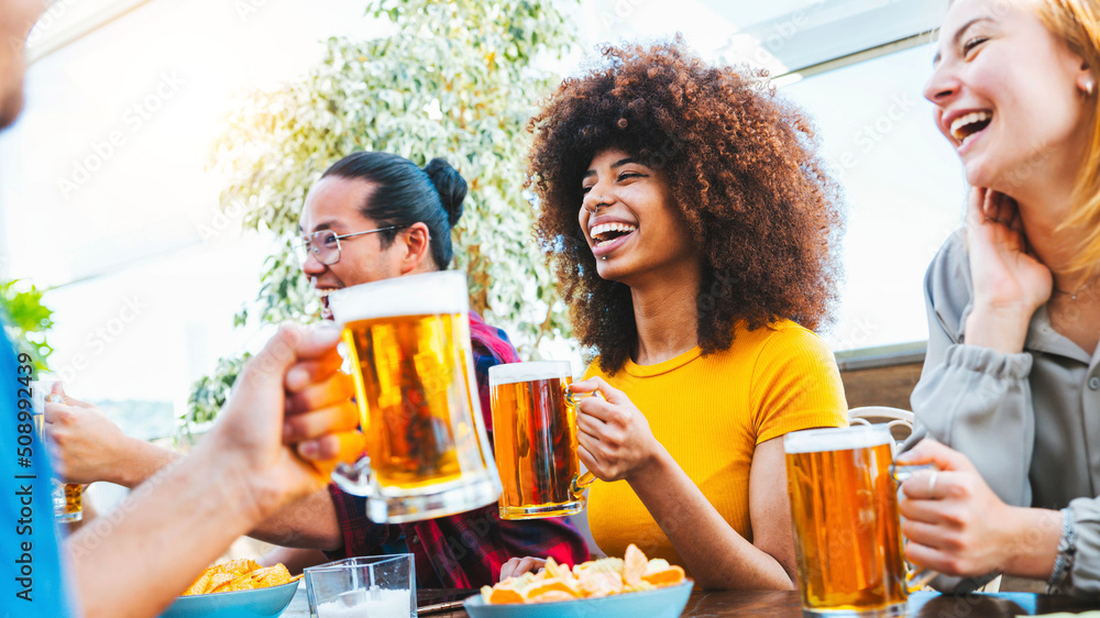 快乐的多种族朋友在啤酒厂酒吧为啤酒杯欢呼——一群年轻人在用餐