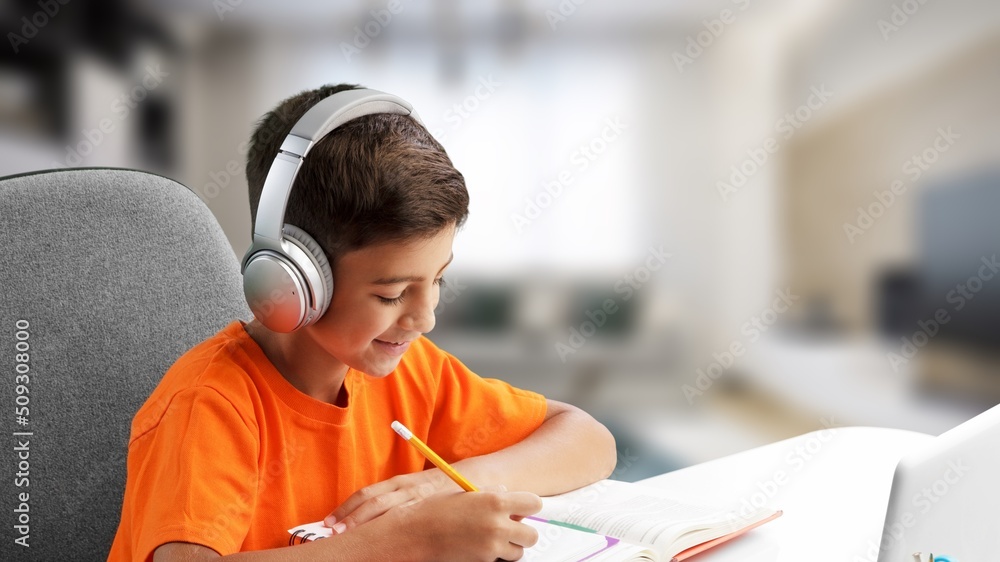 小男孩在家做作业，拿着书和笔坐在桌子旁