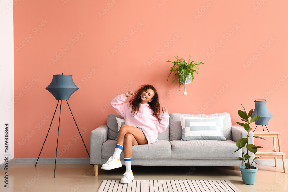 年轻女子在粉色墙壁附近的舒适沙发上放松