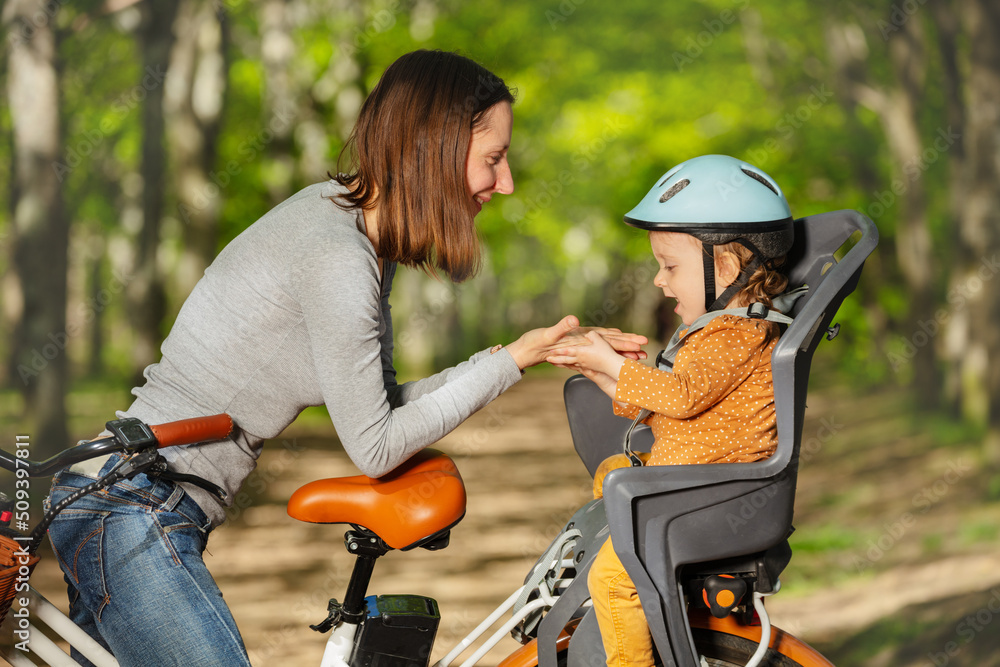 妇女和小女孩在自行车儿童座椅上戴头盔