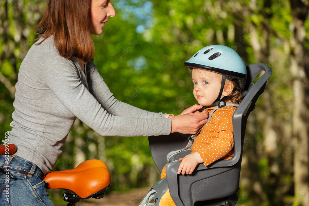 Mother attach helmet to little girl sitting in the bicycle