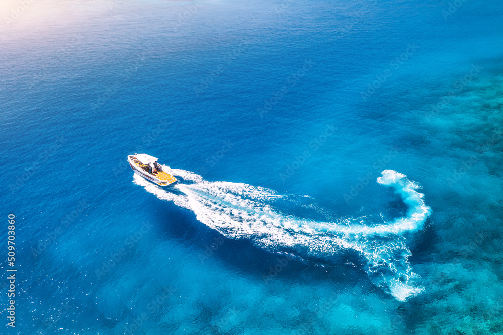 Aerial view of the speed boat in clear blue water at sunset in summer. Top view from drone of fast f