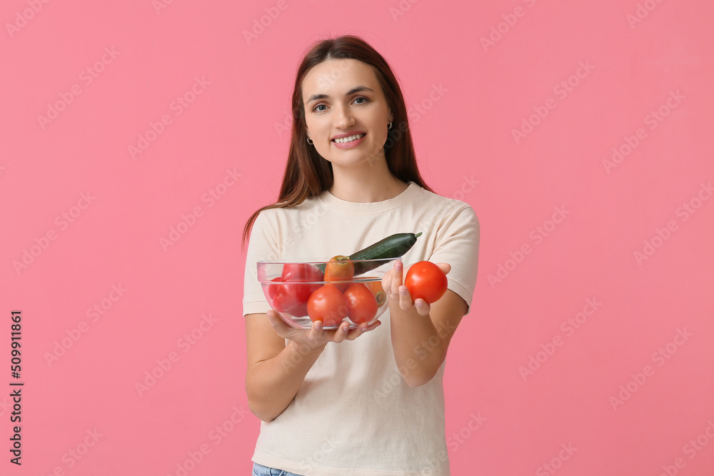 漂亮的年轻女人拿着粉红色背景的新鲜蔬菜的碗