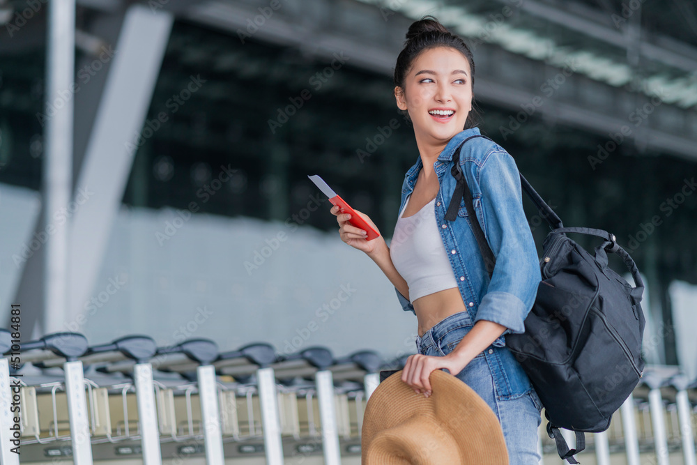 微笑的亚洲女性放松无忧无虑的休闲布走在机场手里拿着登机牌和行李