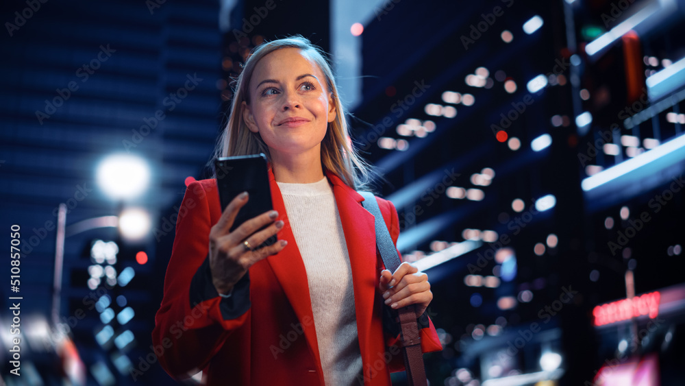 Portrait of a Beautiful Woman in Red Coat Walking in a Modern City Street with Neon Lights at Night.