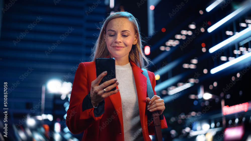 Portrait of a Beautiful Woman in Red Coat Walking in a Modern City Street with Neon Lights at Night.