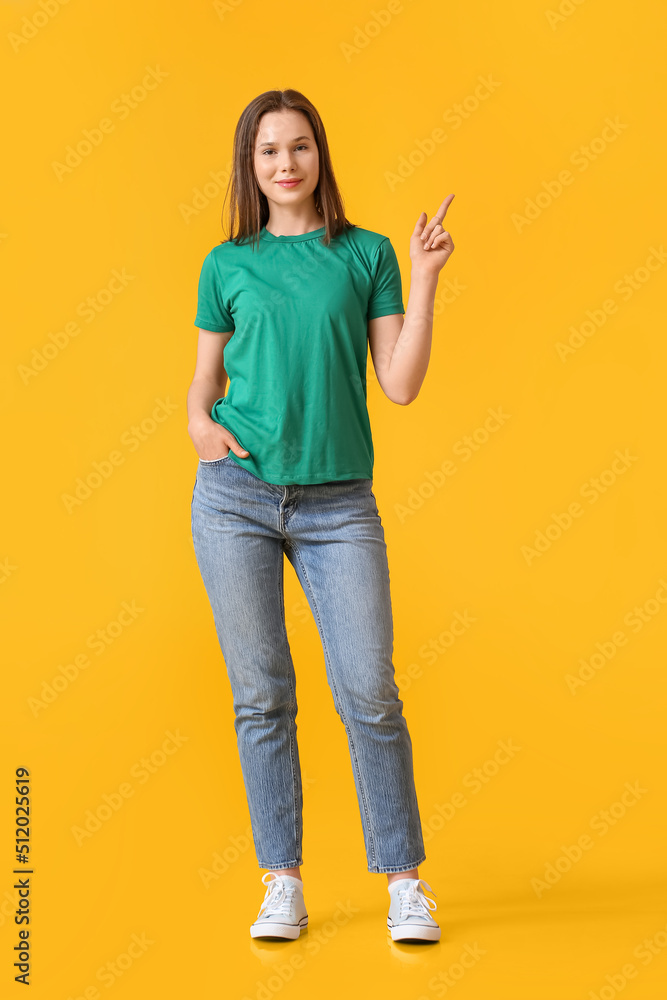 穿着绿色t恤的漂亮年轻女子指着黄色背景上的东西