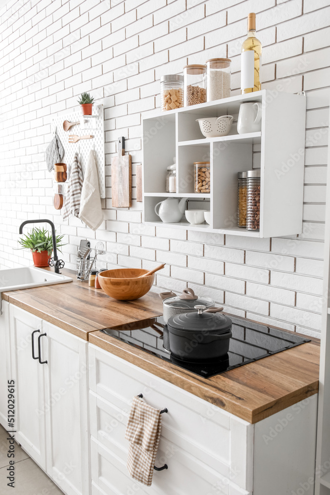 Shelf unit with jars and kitchen counters with utensils near white brick wall