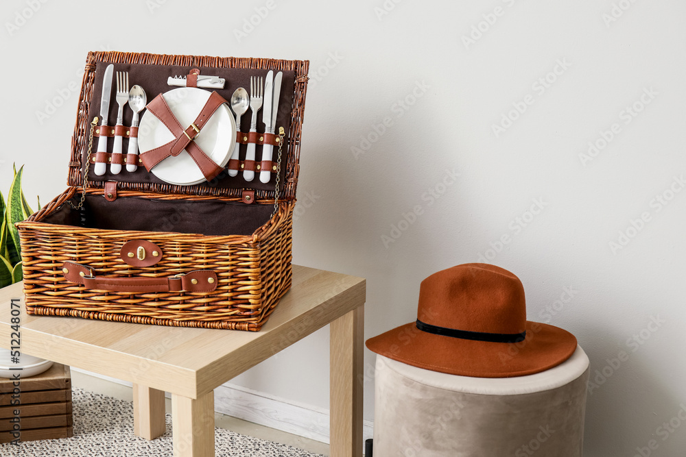 野餐用篮子放在桌子上，带帽子的袋子靠近浅色墙壁