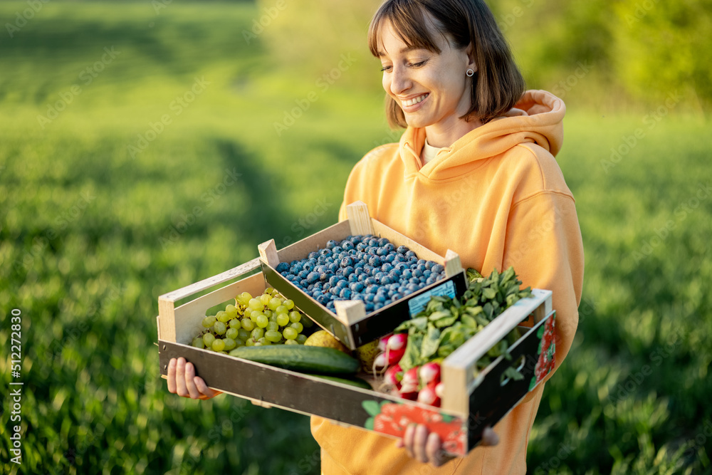 兴高采烈的女人在农田里拿着装有新鲜多汁浆果、水果和蔬菜的盒子。概念o