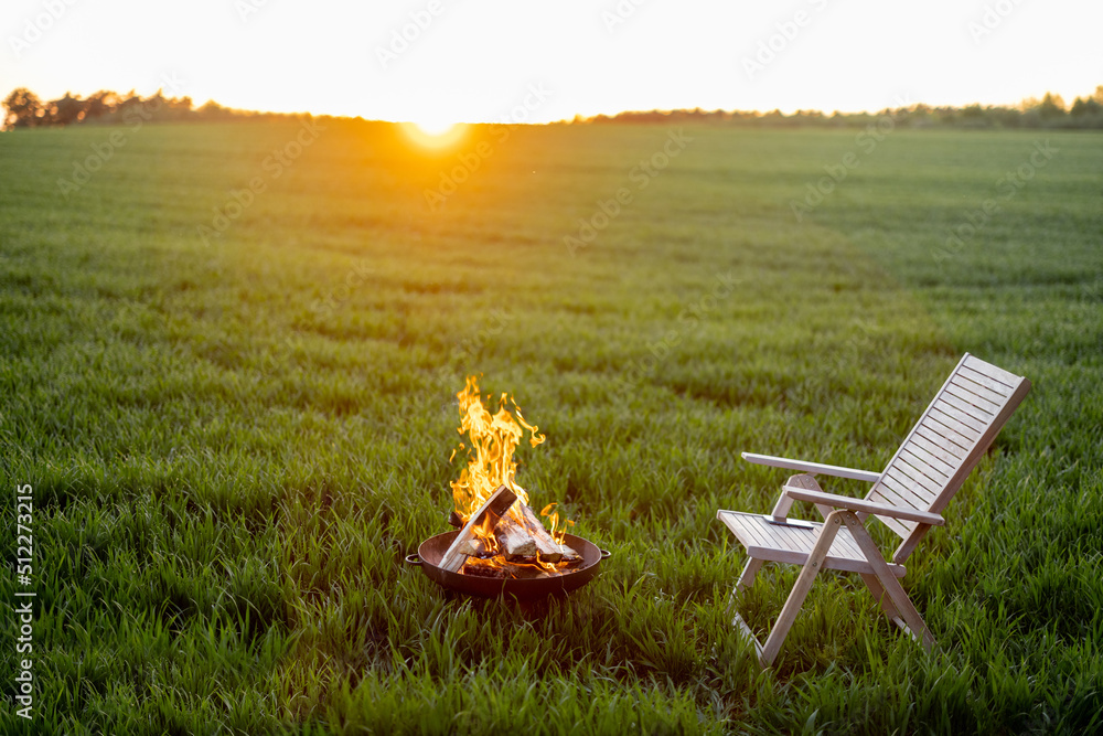 日落时，绿色麦田上有一个漂亮的壁炉和木椅。逃离的概念