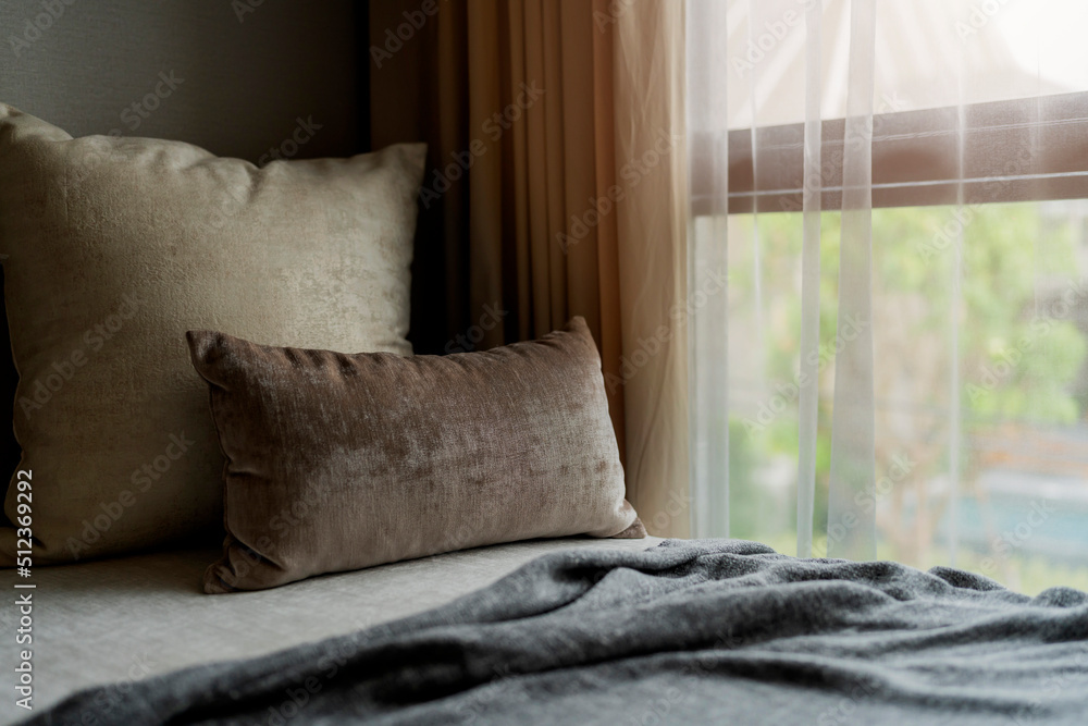 带黄色米色枕头的单人床垫，布置在白色窗帘、遮阳帘和风旁边