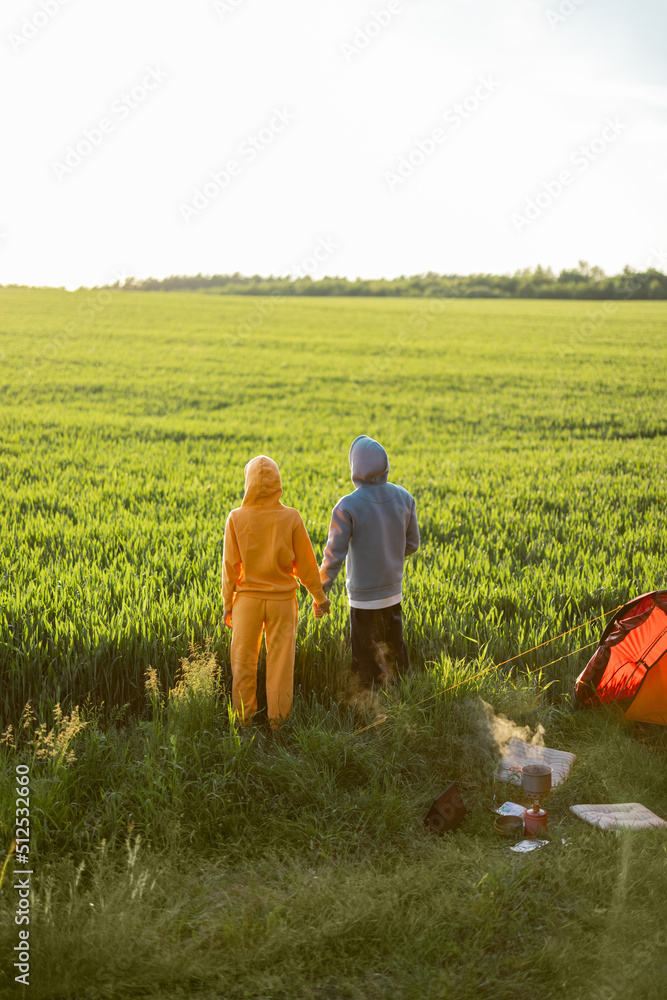 年轻夫妇带着帐篷在大自然中旅行，欣赏日落美景。男人和女人