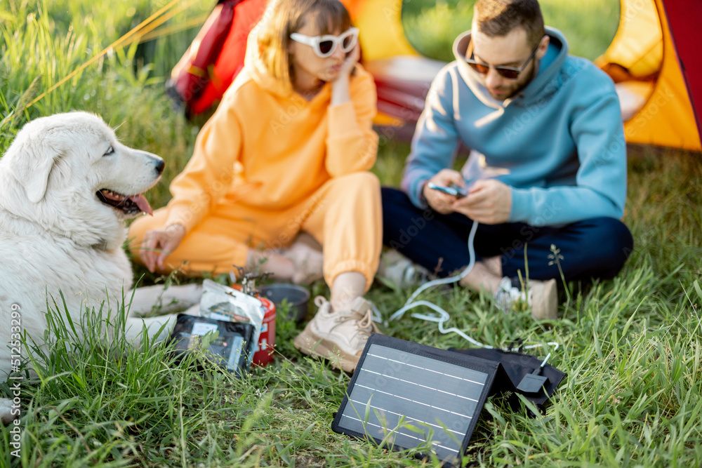 一男一女在露营地和狗坐在一起，在大自然中旅行。用便携式溶胶为小工具充电