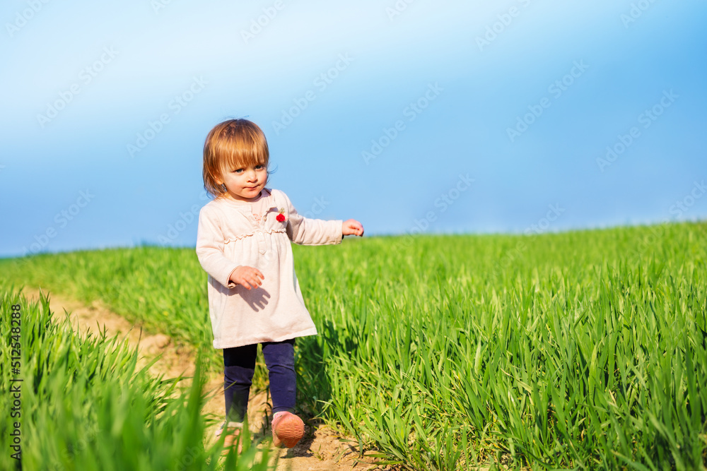 穿着粉色连衣裙的幼童在清澈的春天田野上奔跑