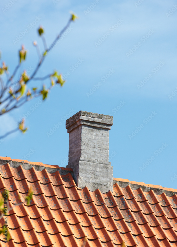 灰色砖砌烟囱，在蓝天背景下，设计在房屋建筑的石板屋顶上。Con