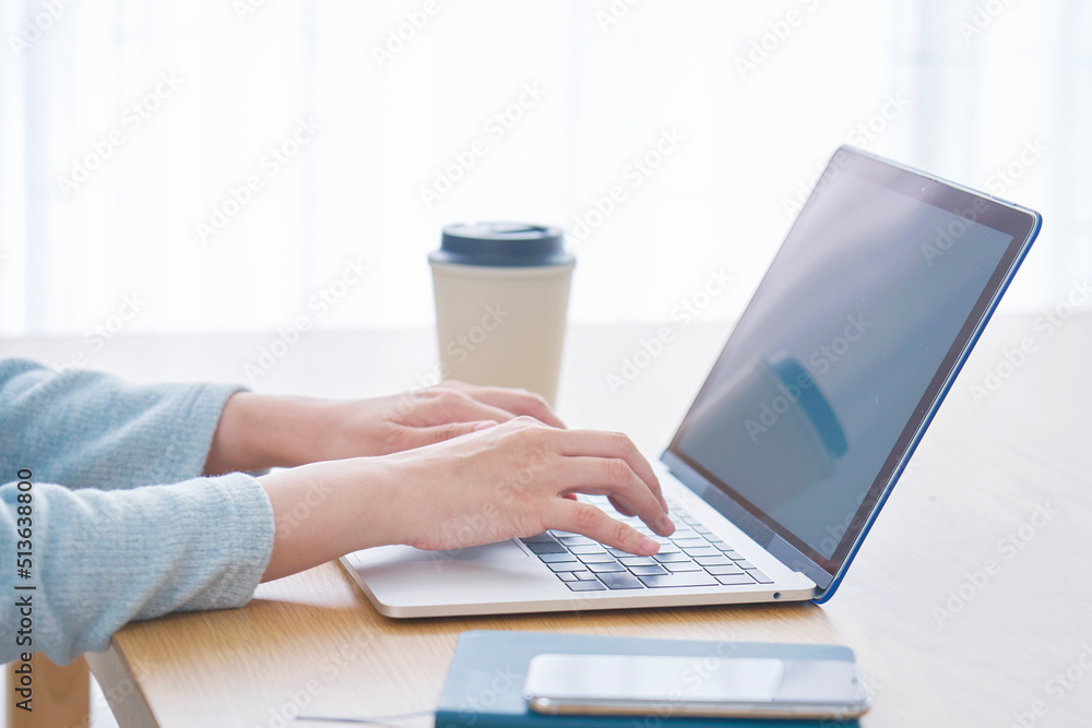 リビングでノートパソコンのをタイピングする女性の手元