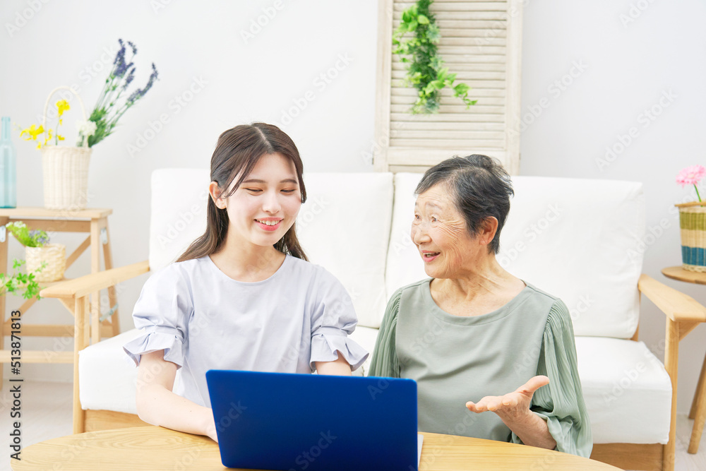 リビングでノートパソコンの前で会話する孫と祖母