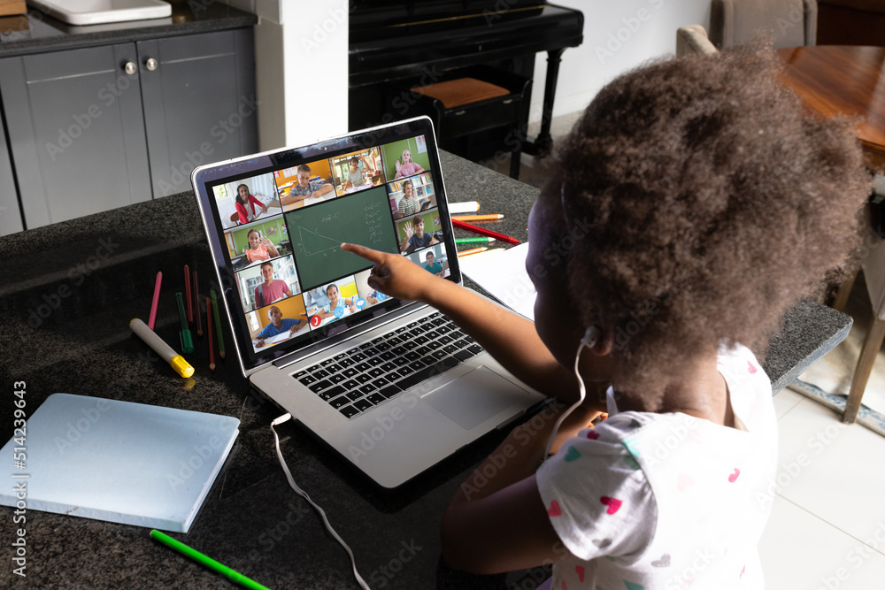 留着非洲头发的非裔美国女孩在家上网课时指着笔记本电脑屏幕