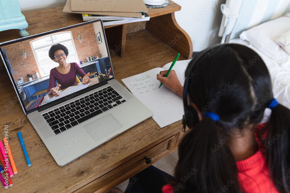混血女孩在写英语，而非裔美国女子在笔记本电脑上通过视频通话在线教学