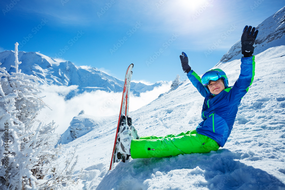 男孩滑雪者坐在雪中翻越山峰举起双手