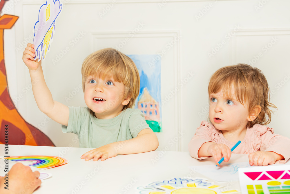 男孩和一个女孩坐在幼儿园课堂上展示天气卡