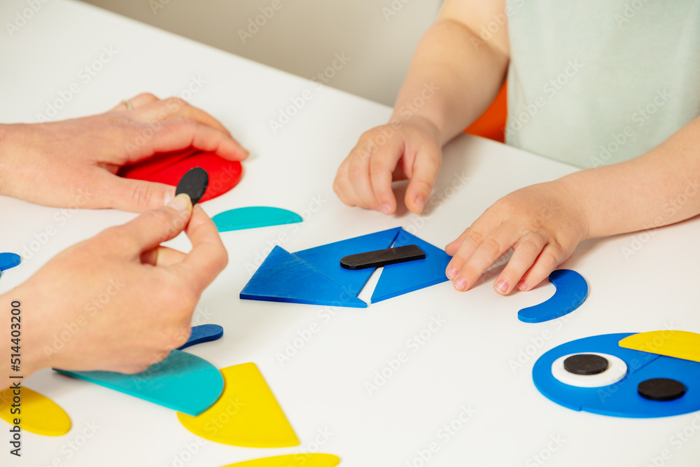 Adult help little child put shapes in form of a house