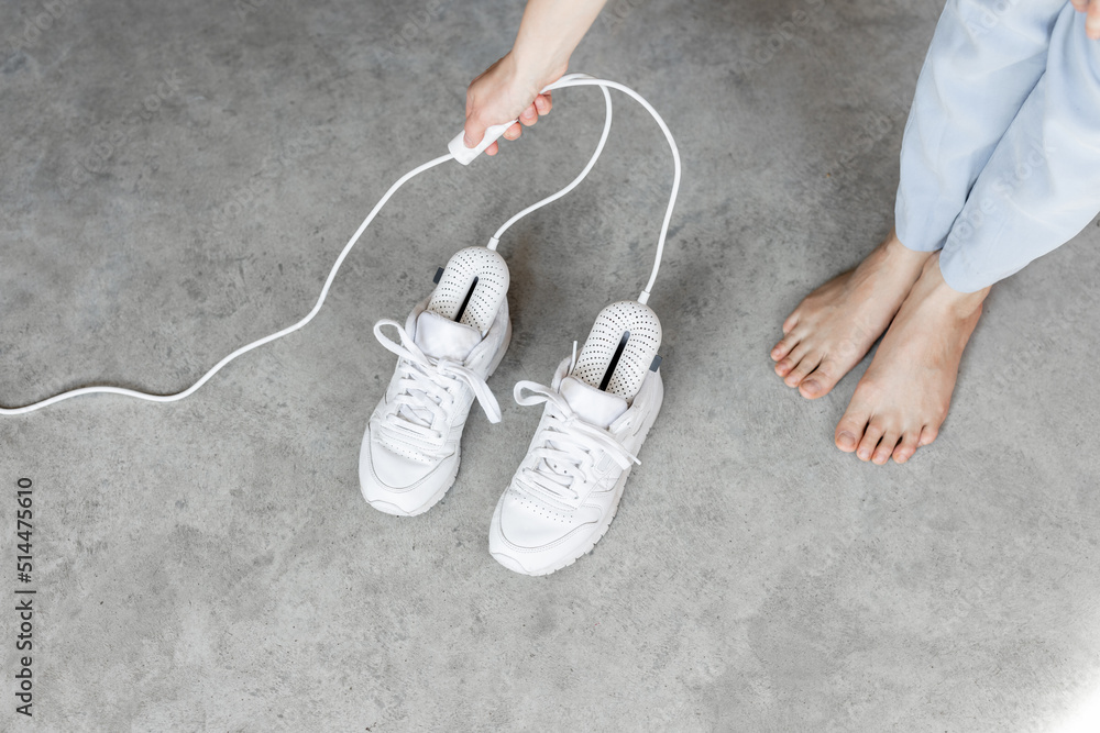 女人打开电动鞋烘干机烘干她的白色运动鞋，特写地板上的鞋子。Concep