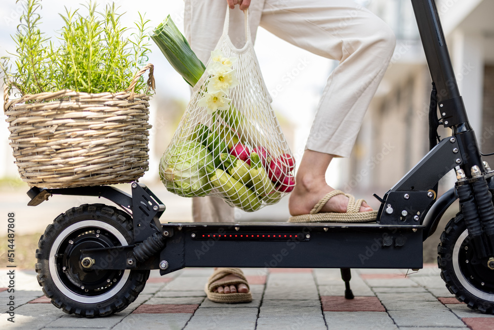 一名女子拿着装满新鲜蔬菜的网袋，准备用迷迭香开电动滑板车