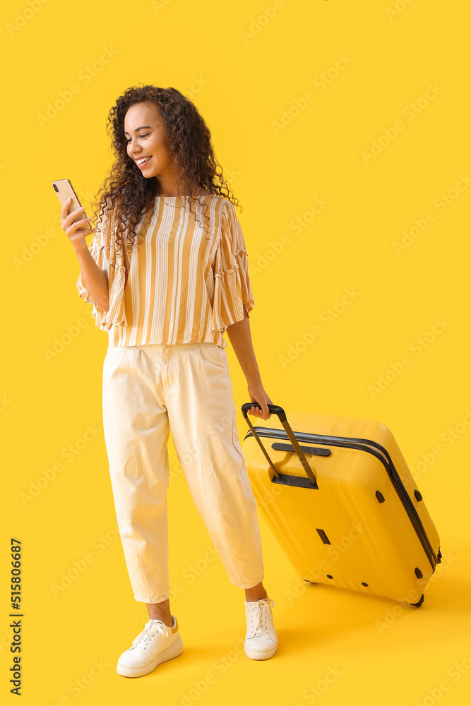 年轻的非裔美国妇女拿着黄色背景的行李箱用手机