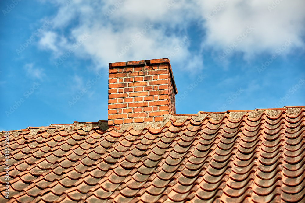 Red brick chimney designed on the roof of residential house or building outside against a cloudy sky
