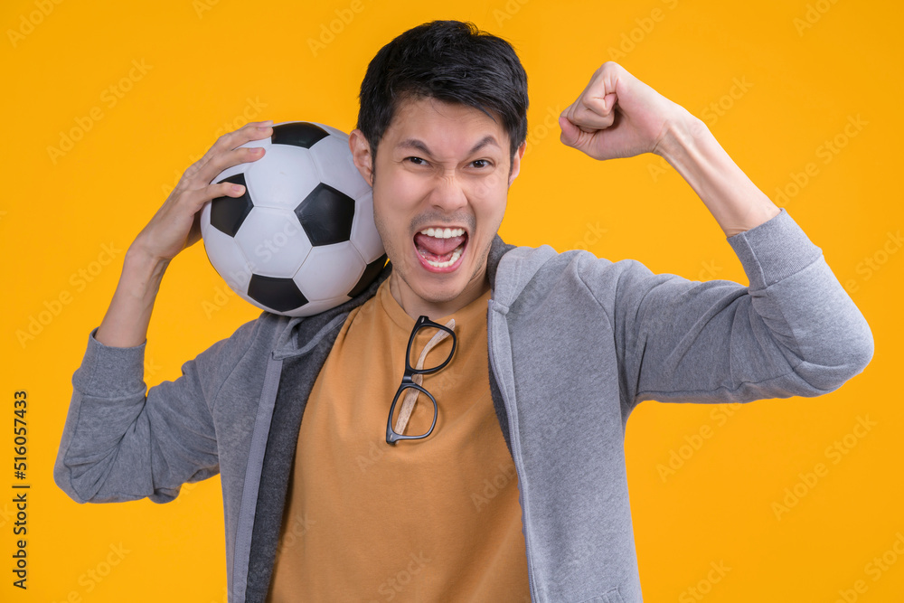兴奋的亚洲成年男子足球迷戴着黄色t恤，为手中最喜爱的球队加油