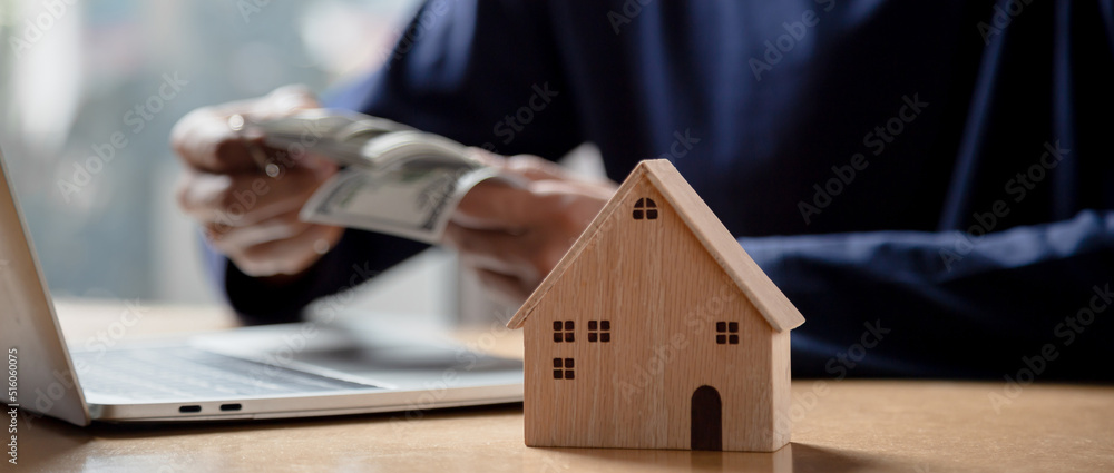 男人手里拿着房子模型，计算投资购买房产的财务图表。