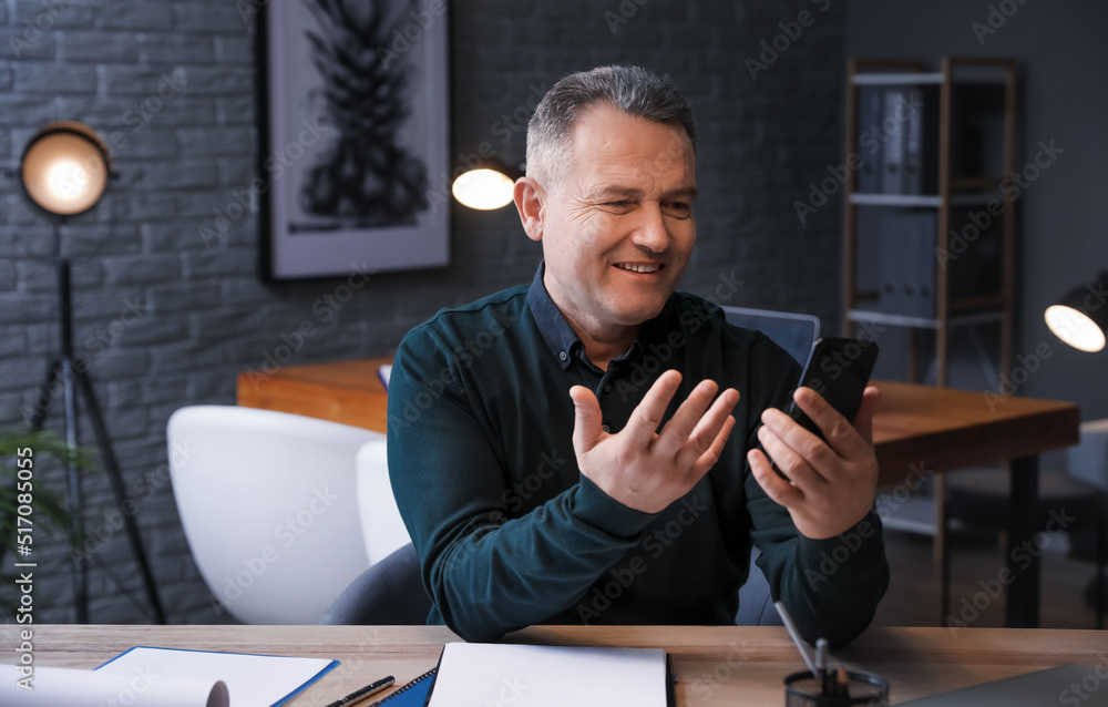 Happy mature man with mobile phone video chatting late in evening