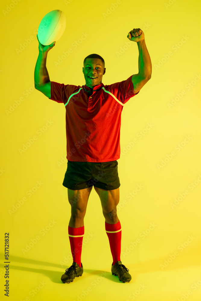 快乐的非裔美国男子橄榄球运动员在黄色灯光下举手的肖像