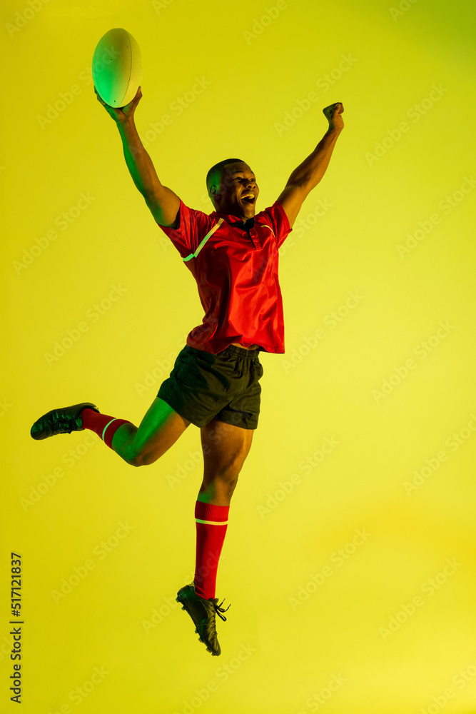 快乐的非裔美国男子橄榄球运动员在黄色灯光下举手
