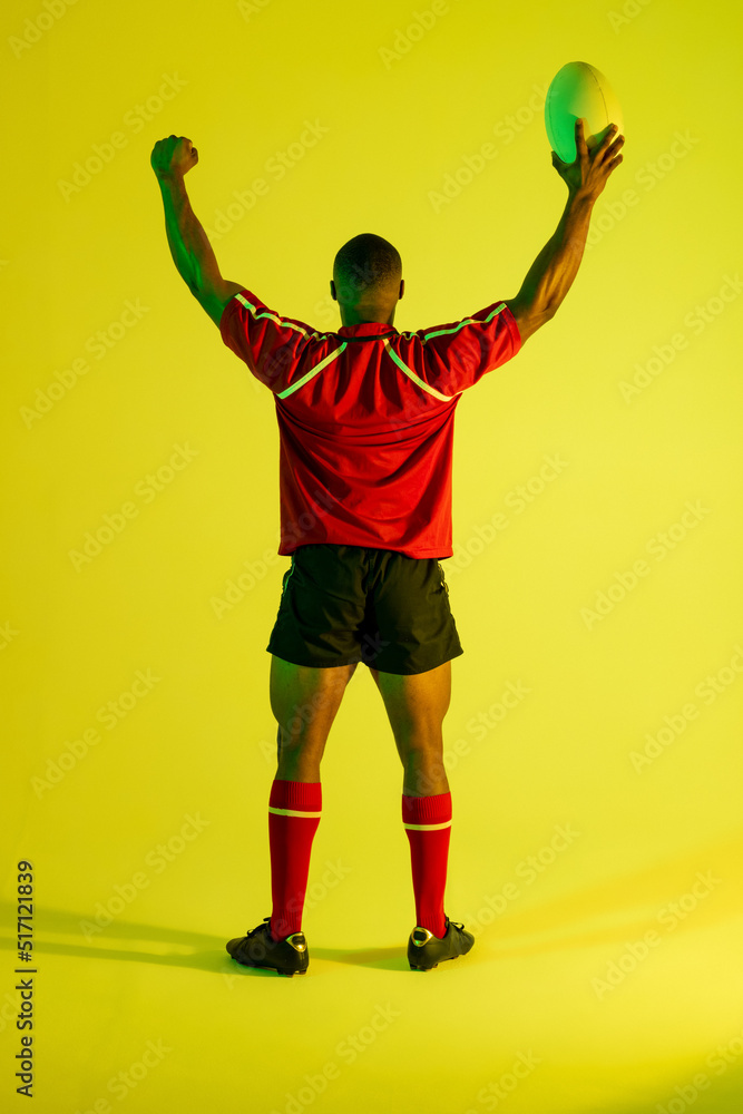 非裔美国男子橄榄球运动员在黄色灯光下举手