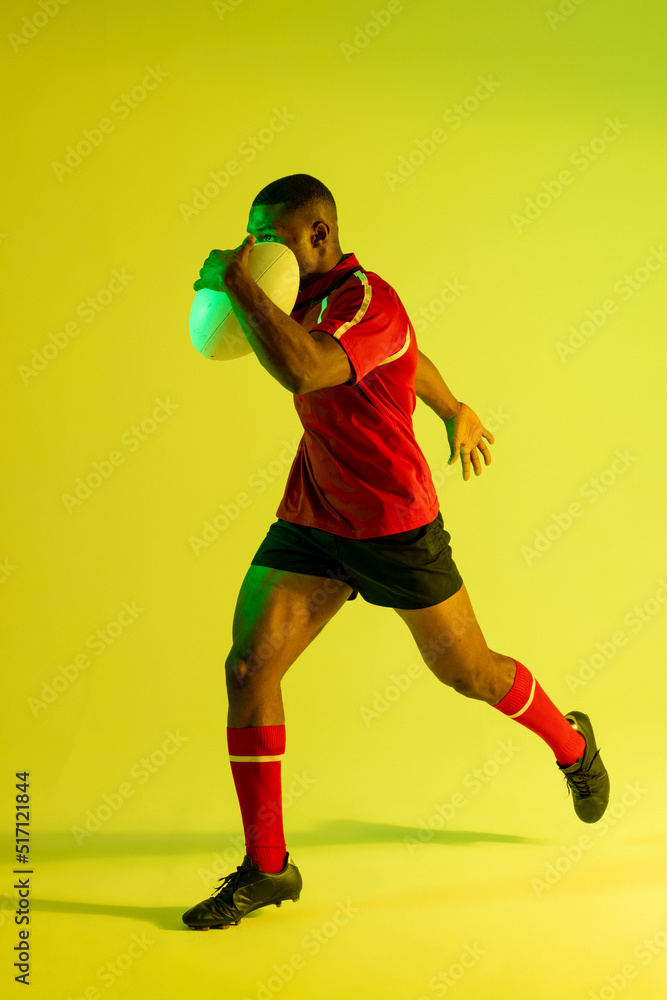 非裔美国男子橄榄球运动员拿着橄榄球在黄色灯光下奔跑