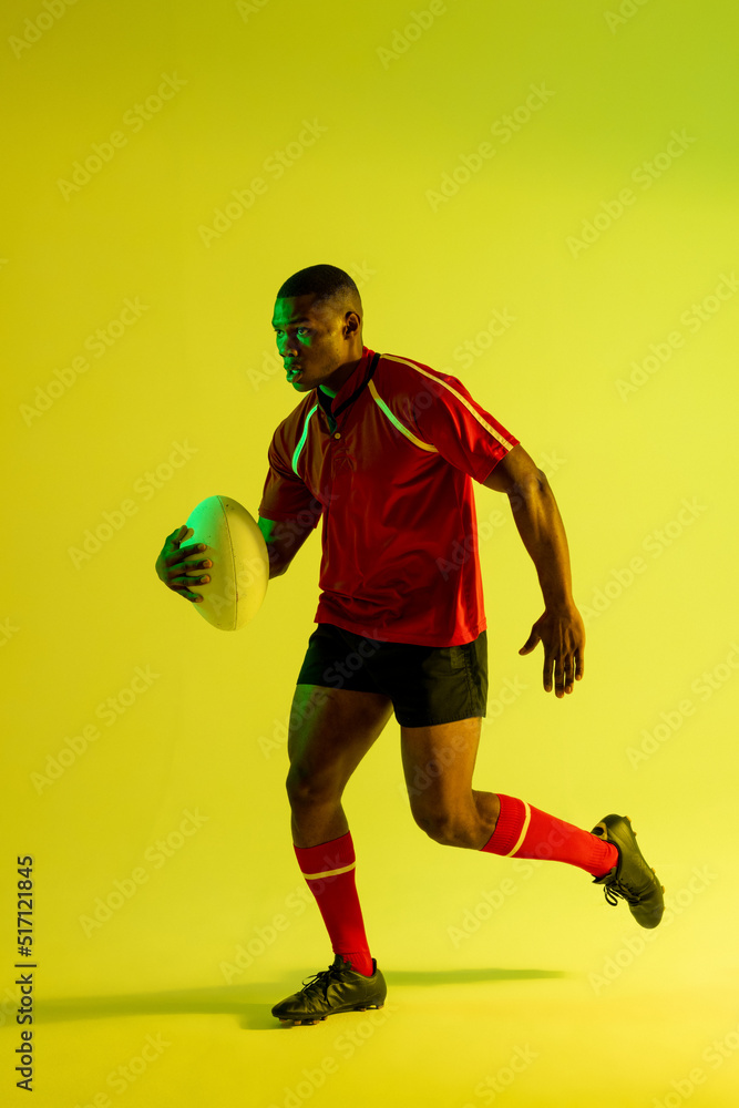 非裔美国男子橄榄球运动员在黄色灯光下拿着橄榄球奔跑
