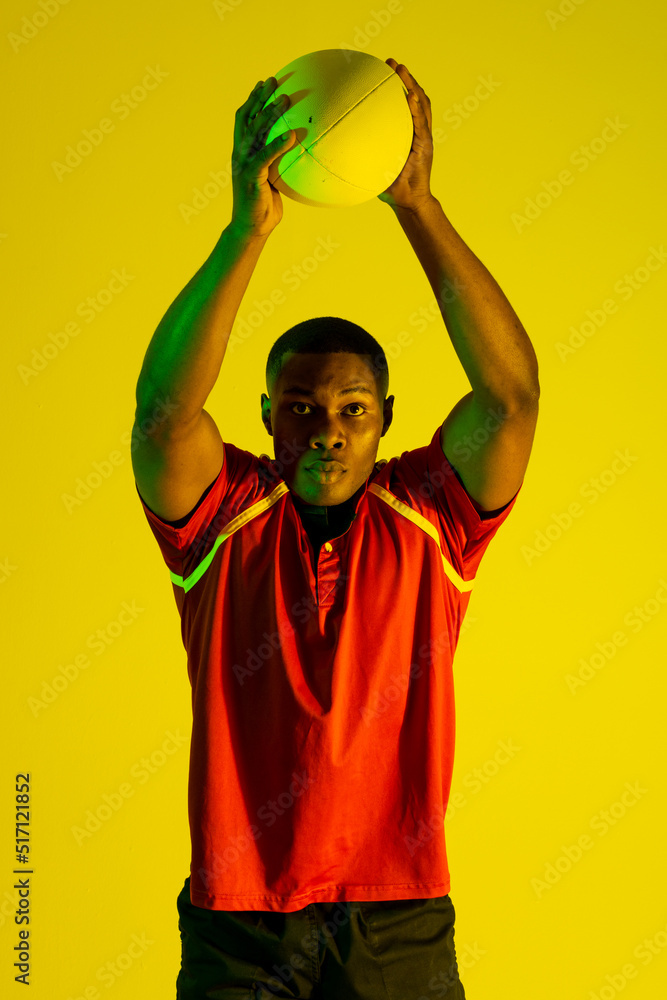 黄色灯光下拿着橄榄球的非裔美国男子橄榄球运动员的肖像