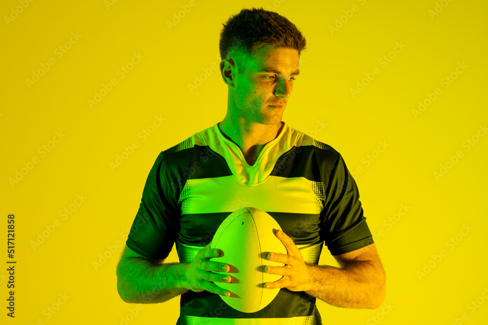 高加索男子橄榄球运动员在黄色灯光下拿着橄榄球